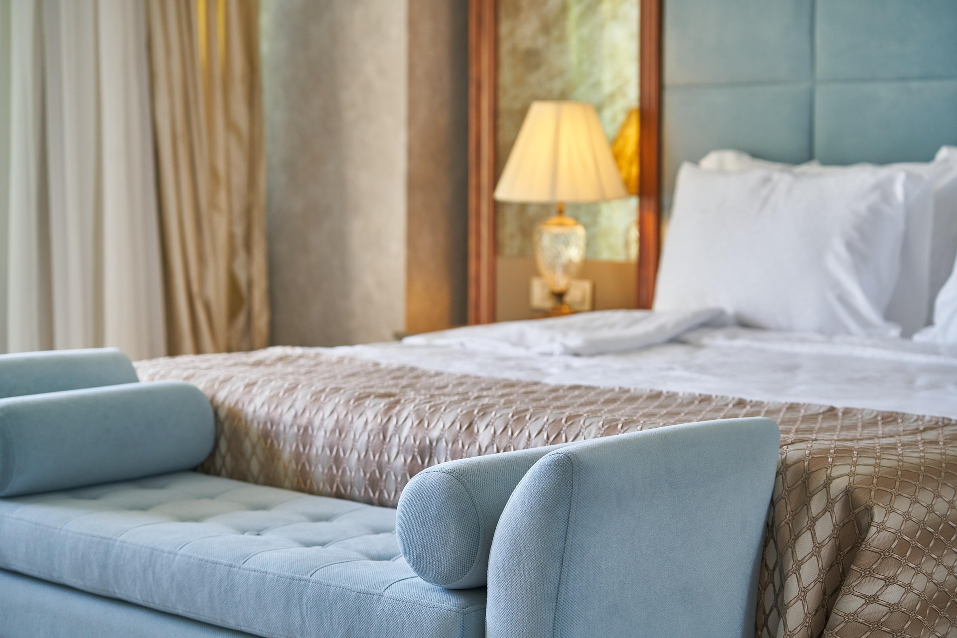 Habitación de hotel de estilo elegante con cama de matrimonio, ropa de cama blanca y decoración en tonos azules y dorados